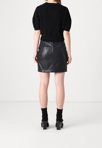 Svart kortärmad tröja kombinerad med en figurnära svart läderkjol. Kjolen har en dragkedja i ryggen och en mjuk textur. Svarta blockklackskor.