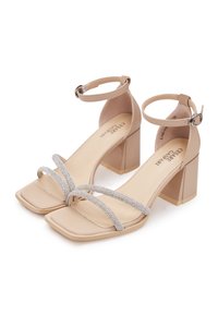 Sandales à talons carrés beige avec un orteil carré, dotées de deux fines lanières ornées de strass et d'une lanière de cheville avec une boucle en argent.