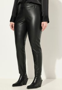 Zwarte neplederen leggings met een hoge tailleband, een gladde textuur en een taps toelopende pasvorm, gecombineerd met zwarte enkellaarzen met hakken versierd met zilveren studs.