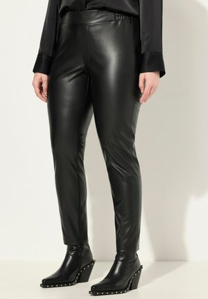 Leggings en similicuir noirs avec une taille haute, texture lisse et coupe fuselée, associés à des bottines noires à talons ornées de clous en argent.