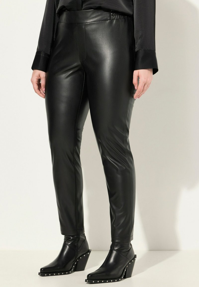 Zwarte neplederen leggings met een hoge tailleband, een gladde textuur en een taps toelopende pasvorm, gecombineerd met zwarte enkellaarzen met hakken versierd met zilveren studs.