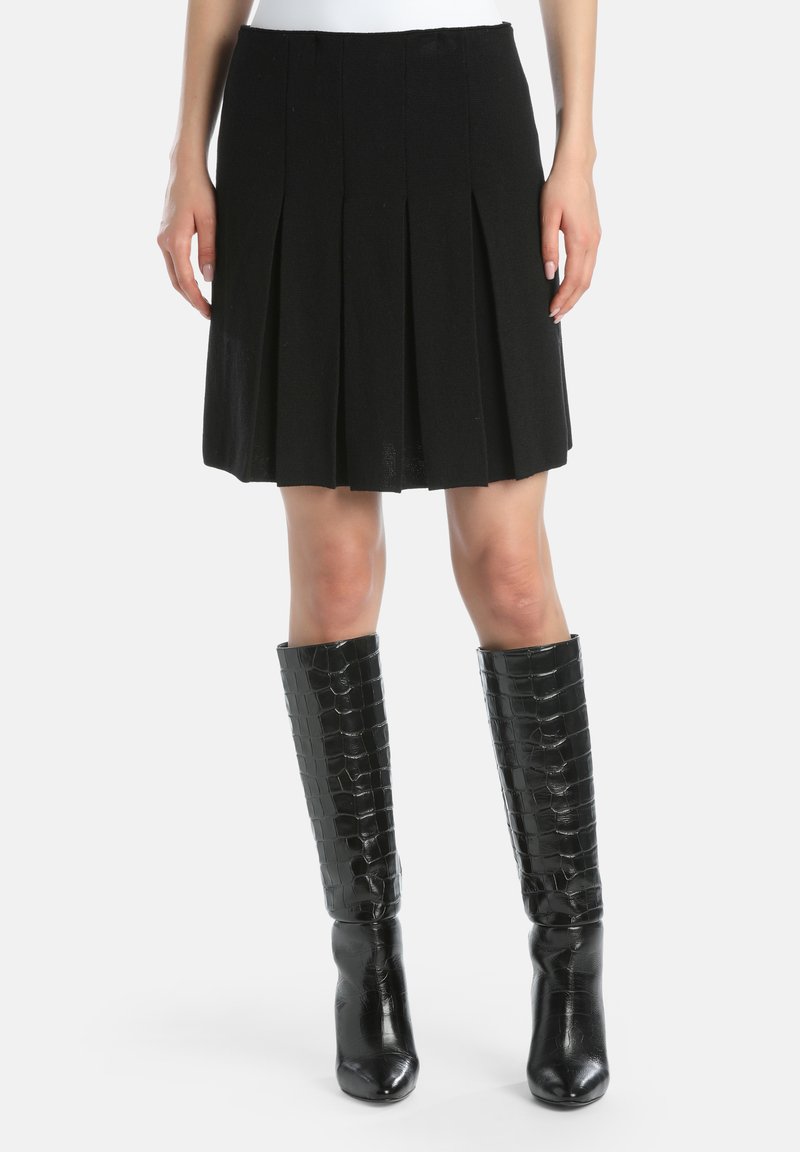 Zwarte geplooide rok van textiel, gecombineerd met kniehoge glanzende zwarte laarzen met een krokodillenpatroon en scherpe hakken.