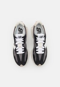 Svarta och grå sneakers med en blandning av mocka och mesh-material, vita snören, med en distinkt vit logotyp och texturerad sula.