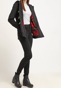 Cappotto nero con cappuccio e chiusure a toggles, fodera in tartan rosso, abbinato a un top grigio, jeans skinny neri e stivaletti neri con tacco chunky.