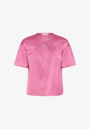 Mīksta rozā zīda blūze ar īsām pūkainām piedurknēm, apaļu kakla izgriezumu un smalkām priekšējām krokām, attēlota uz balta fona.