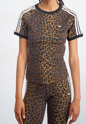 Femme portant un t-shirt Adidas marron et noir imprimé léopard et un legging assorti avec des rayures blanches sur les manches et les côtés.