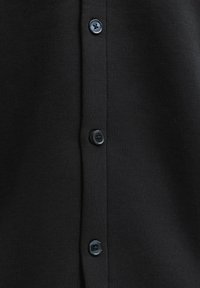 Gros plan d'un tissu noir avec quatre boutons noirs alignés verticalement sur une patte boutonnée.