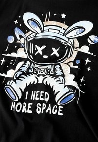 Camiseta negra con un conejo de dibujos animados en un traje de astronauta, con acentos en blanco y azul. El texto dice: "NECESITO MÁS ESPACIO."