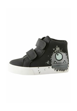 Chaussure montante noire avec des bandes Velcro, dotée d'une semelle en caoutchouc blanche et d'un design graphique de monstre en gris avec un seul œil.