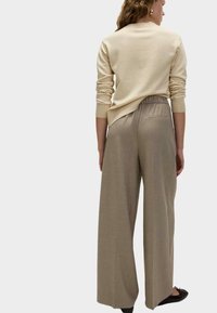 Cremfarbener Pullover mit gerippten Bündchen, kombiniert mit hochtaillierten, weit geschnittenen taupefarbenen Hose mit einer Gesäßtasche und glatter Textur. Schwarze Ballerinas.