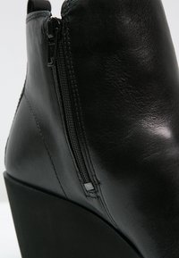 Bottine en cuir noir à talon compensé, avec une fermeture éclair latérale et une texture lisse. Design minimaliste avec une silhouette épurée.