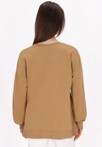 Felpa oversized marrone con maniche lunghe e polsini a costine. Presenta un collo rotondo e un tessuto morbido e testurizzato.