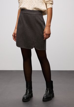 Grå ullblandning minikjol med en scalloped nederkant, tillsammans med svarta ankelstövlar och genomskinliga svarta strumpbyxor. Enkelt mönster, slät textur.