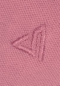 Roze gebreide textiel met een iets verheven, geborduurd, driehoekig logo in een bijpassende schaduw van roze. Zachte textuur met een gelijkmatig patroon.