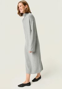 Abito grigio a maniche lunghe con collo alto in tessuto rigato, lunghezza fino al polpaccio, abbinato a ballerine nere. Design semplice, vestibilità rilassata, senza patterned.