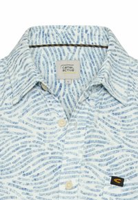 Overhemd met kraag, witte basis en blauw abstract golfpatroon, beige knopen, en Camel Active merklabel op het borstzakje en aan de binnenkant van de kraag.
