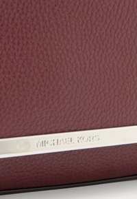 Pelle martellata bordeaux con placca logo in argento. Texture liscia con una leggera lucentezza. Forma rettangolare moderna, design minimalista.