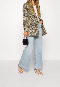 Beige and black animal print blazer over a white top, paired with light blue wide-leg jeans and white heeled sandals. Small black handbag accent.