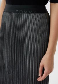 Gonna nera a pieghe con una texture elegante, dotata di un ampio elastico in vita stampato con la parola "COMMA" in un colore abbinato.