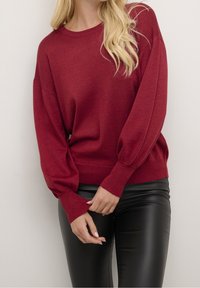 Pull-over bourgogne avec des manches longues bouffantes, des poignets côtelés et un ourlet. Assorti à un pantalon en cuir noir. Tissu doux et texturé.