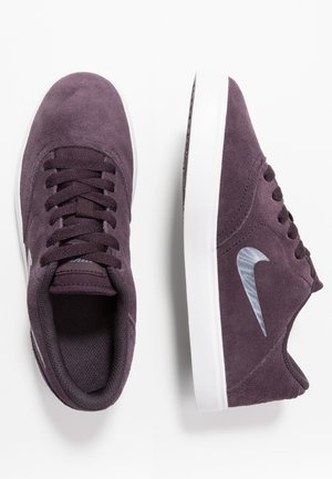 Para ciemnofioletowych zamszowych sneakersów Nike z białą podeszwą, jeden pokazuje widok z góry z sznurowadłami, drugi widok boczny ze srebrnym logo Nike swoosh.