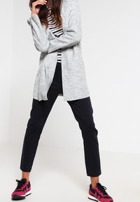 Cárdigan gris texturizado sobre una camiseta de rayas negras y blancas, combinado con pantalones azul marino y zapatillas rosas y negras.