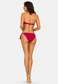 Czerwony zestaw bikini z topem bandeau i dołami z wiązaniem po bokach. Gładki, elastyczny materiał; minimalistyczny dizajn bez widocznych wzorów i okuć.