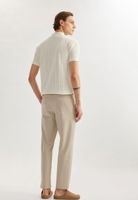 Lichtgewicht gebreide polo in crème met verticale strepen, gecombineerd met beige broeken. Schoenen zijn lichtbruine instappers; casual, relaxte pasvorm.