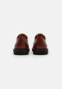 Brune lærstøvler med en glat overflade, rundt tåparti og sort gummisål. Har minimal syning og et slip-on design med en diskret hæl.