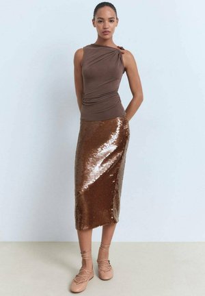 Haut marron ajusté avec un design asymétrique, associé à une jupe crayon en sequins bronze. Le modèle porte des ballerines nudes à lacets. Textures lisses.