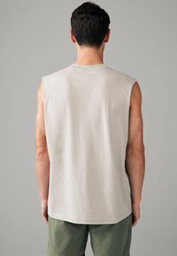 Mouwloos lichtbeige T-shirt van zachte katoen, met een ronde halslijn en een licht gebogen zoom, gecombineerd met groene shorts.