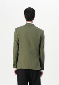 Blazer gris carbón con corte ajustado, hecho de tejido texturizado. Presenta solapas delgadas y puños abotonados. Abertura en la parte trasera para facilitar el movimiento.
