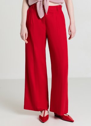 Pantaloni rossi a gamba larga, su misura, con pieghe frontali e una texture liscia. Abbinati a ballerine rosse coordinate e una maglia a righe.