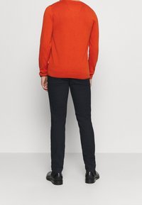 Červený pletený svetr s dlouhými rukávy, žebrovanými manžetami a lemem. Spárován s tmavě modrými slim-fit kalhotami a černými kotníkovými botami.