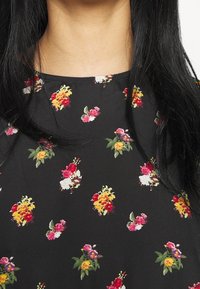 Svart tyg med ett blommönster som har små röda, gula och vita blommor. Slät textur och rund halsringning.