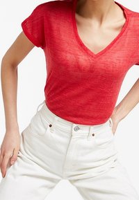 T-shirt rossa con scollo a V e maniche corte, realizzata in tessuto leggero. Abbinata a jeans bianchi a vita alta, colori e trame a contrasto.