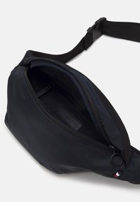 Borsa a vita nera in nylon con scomparto principale con zip e una piccola tasca esterna. Include logo distintivo e tracolla regolabile.