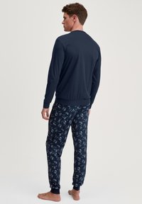 Marineblauwe lange mouwen top gecombineerd met marineblauwe broek met een wit grafisch patroon. De broek heeft elastische boorden; de top heeft een geribde kraag en zoom.