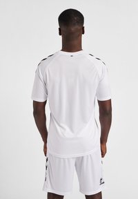 Maillot de sport blanc à manches courtes, avec des accents noirs sur les épaules et un logo sur le bas à gauche. Texture de tissu lisse.