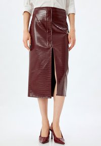 Burgundy faux leather nederdel med krokodillesktexture, knælængde, med en frontslids og en glat finish, parret med matchende hæle.