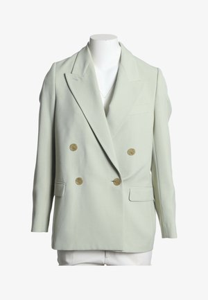 Veste croisée vert clair avec larges revers et quatre boutons marron, exposée sur un buste de mannequin blanc.