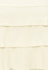 Υφασμα σε κρεμ χρώμα με τρία οριζόντια βολάν και ομαλή υφή.