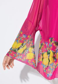 Kimono trasparente rosa con maniche lunghe, caratterizzato da una stampa floreale e di limoni colorata ai polsini. Tessuto leggero e fluente.