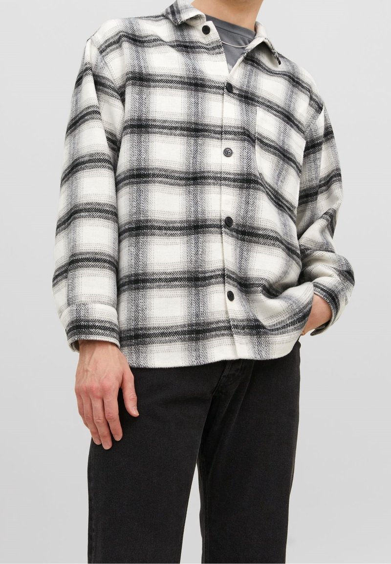 Chemise à carreaux noire et blanche avec une coupe décontractée, présentant de grands motifs à carreaux, un tissu texturé, une fermeture boutonnée à l'avant et un col.