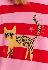 Tričko s horizontálními červenými a růžovými pruhy, se kterým je spojena ilustrace kočky s leopardími skvrnami, černými brýlemi ve tvaru srdce a růžovými hvězdami.
