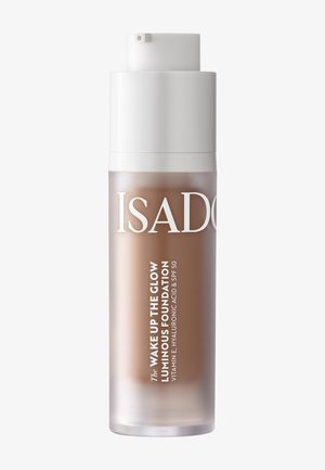 Flacon-pompe transparent du fond de teint lumineux IsaDora Wake Up The Glow avec SPF 50 et vitamine E, acide hyaluronique visible à l'intérieur.