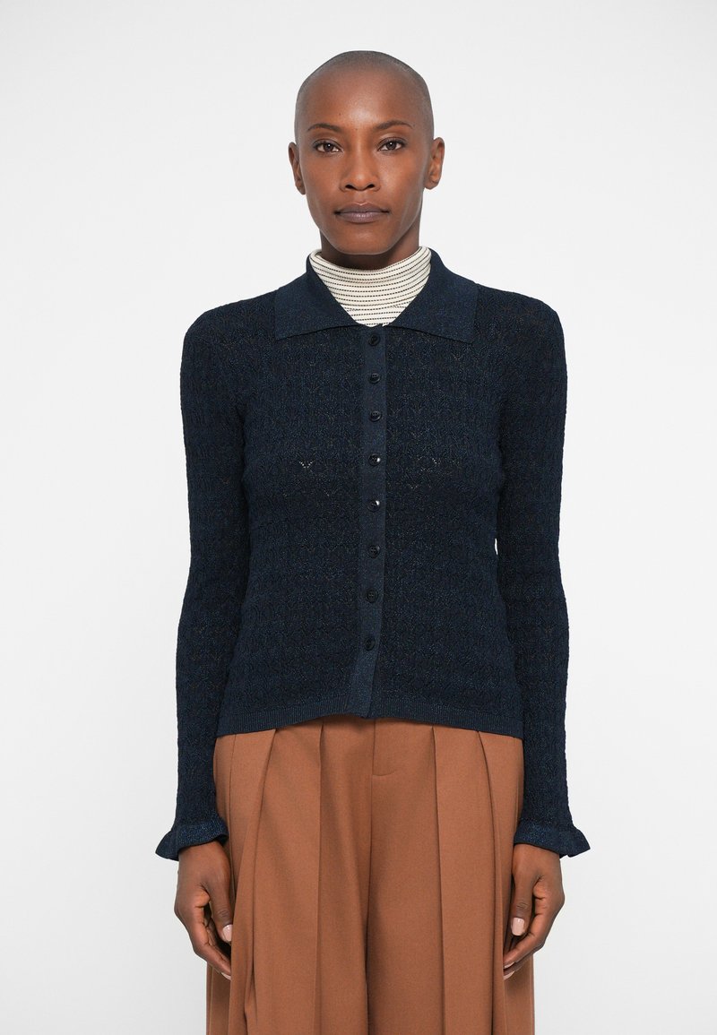 Cardigan en tricot bleu marine avec un motif texturé, fermeture à boutons et col. Manches longues avec des poignets évasés.
