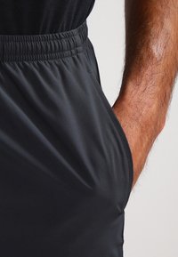 Pantalones cortos deportivos negros con cinturilla elástica, textura suave y bolsillo lateral. Enfocados en un diseño ceñido al cuerpo y material ligero.
