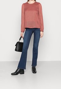 Blusa de color óxido con rayas verticales, mangas fruncidas, combinada con jeans acampanados de color azul oscuro y botines negros, llevando un bolso negro.