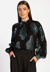 Zwarte blouse met lange mouwen en hoge nek, versierd met een metallic turquoise paisleypatroon, met plissé-details en een zachte textuur, gecombineerd met zwarte broeken.